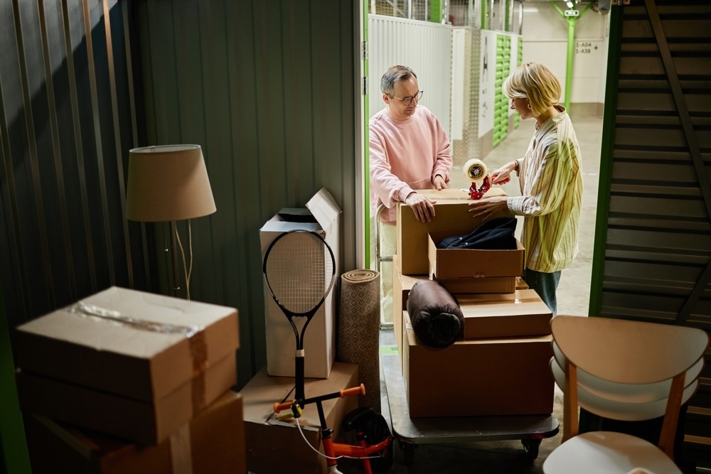 A middle-aged couple moving boxes and furniture into small storage for moving house.